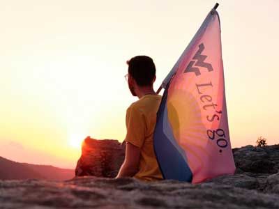 Student holding a WVU flag looking out at a pink sunset.