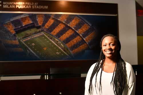Female WVU Sport Management student standing in front of a picture of the football stadium.