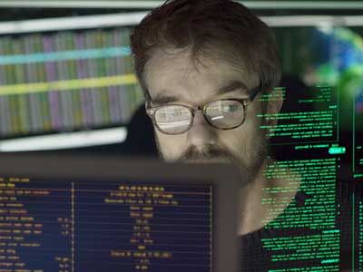 Stock close-up photo of a mature man surrounded by monitors and a holographic display which he is reading.