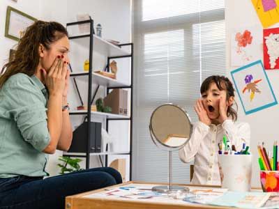 Girl in speech therapy office. Mirror reflection of young girl exercising correct pronunciation with speech therapist.