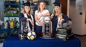 Coach and student athletes posing with NCAA trophies.