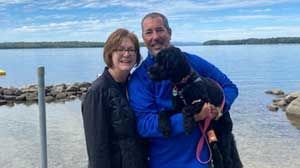 Dave Benedict with his wife and dog in front of a lake.
