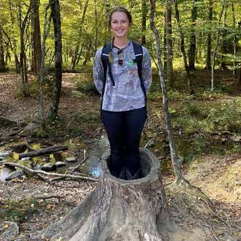 Makenzie Dolly standing on a stump while hiking.