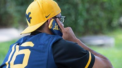 Student wearing a WVU football jersey and backwards WVU hat calling on a cellphone.