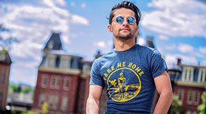 Young man wearing sunglasses and a WVU t-shirt in front of Woodburn.