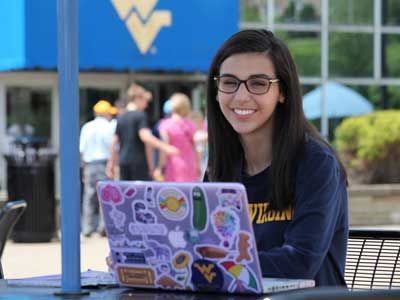 Nicole Andino in front of the Mountainlair on her laptop.
