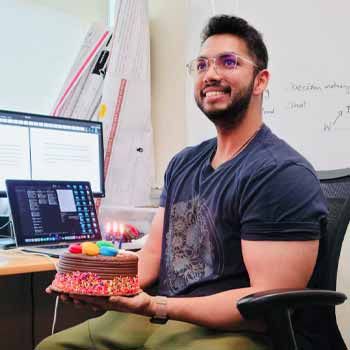 Avishek Choudhury sitting at his desk holding a birthday cake.