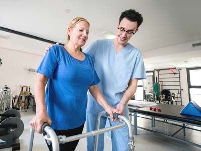 Young man helping a woman with a walker physically rehab.