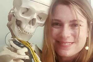 Kelly Ayers posing with a skeleton with a WVU key ring around its neck.
