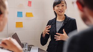 Asian woman talking to coworkers in front of a laptop.