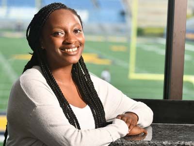 A female Sports Management M.S. graduate sitting in a box at the WVU football field.