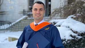 John DeCarlo in his graduation gown holding his cap on a snowy day.