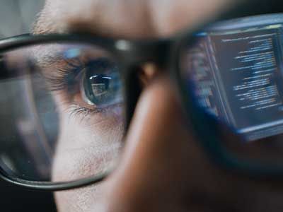 Business cybersecurity worker with numbers reflecting off his glasses.