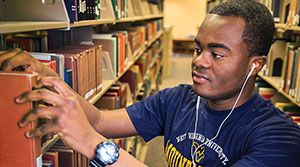 Young man searching through books at the WVU library.
